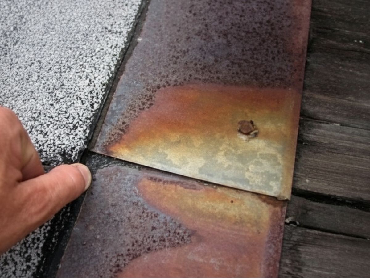 Rusted metal roof flashing with corroded fastener and visible deterioration at shingle edge