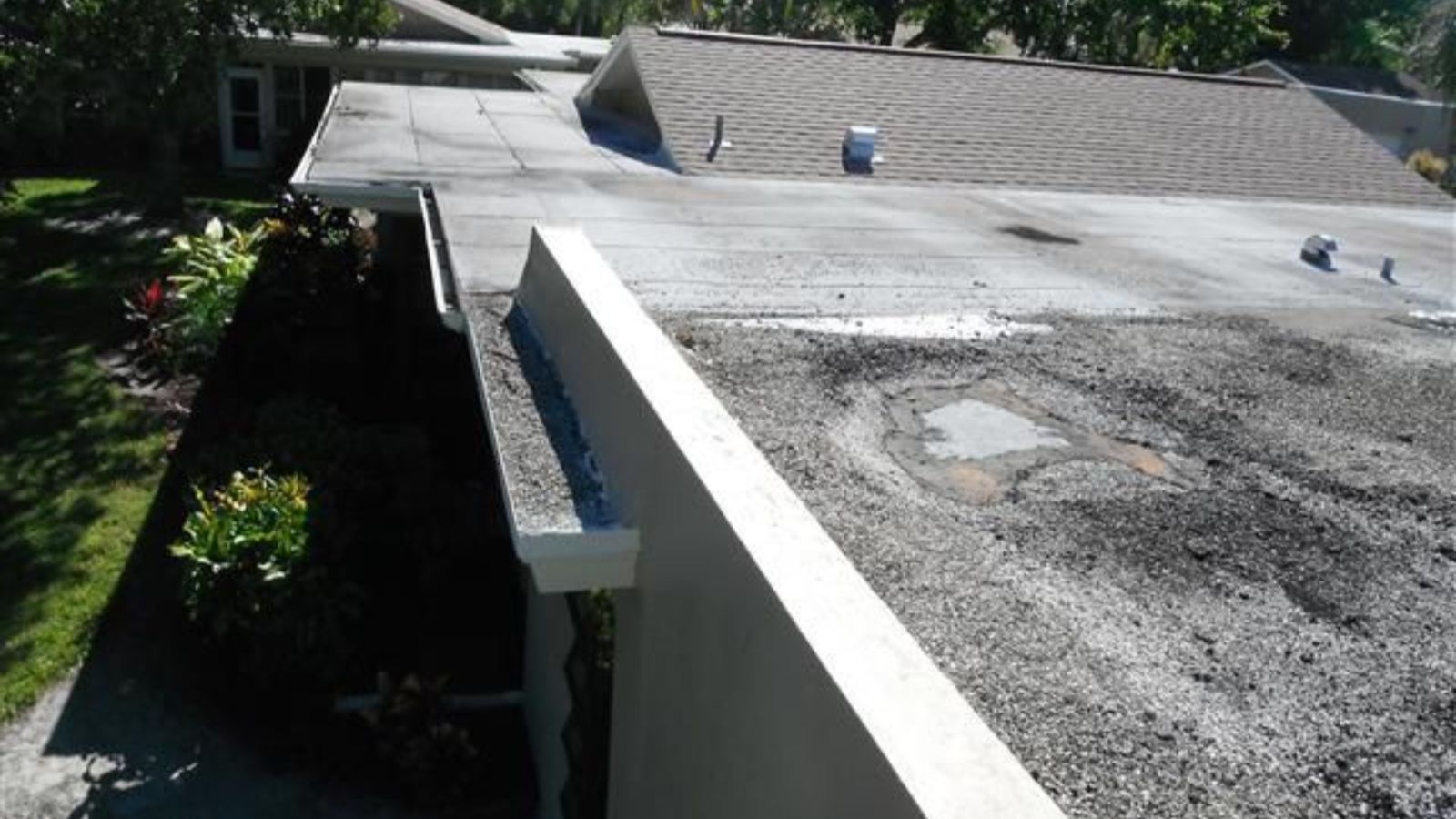 Flat roof with deteriorated surface, ponding water, and patched areas near roof edge and parapet wall