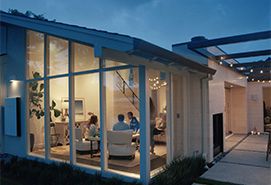 Modern home with large glass walls and covered patio, showcasing bright interior living space during evening hours