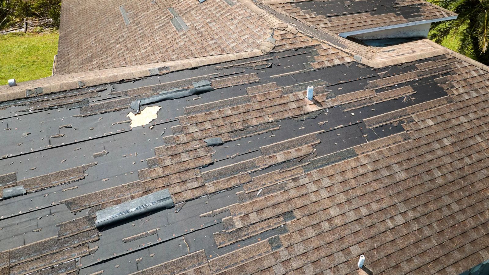 Aerial view of a residential roof with severe asphalt shingle damage, missing shingles, exposed underlayment, and visible roof vents indicating roof deterioration.
