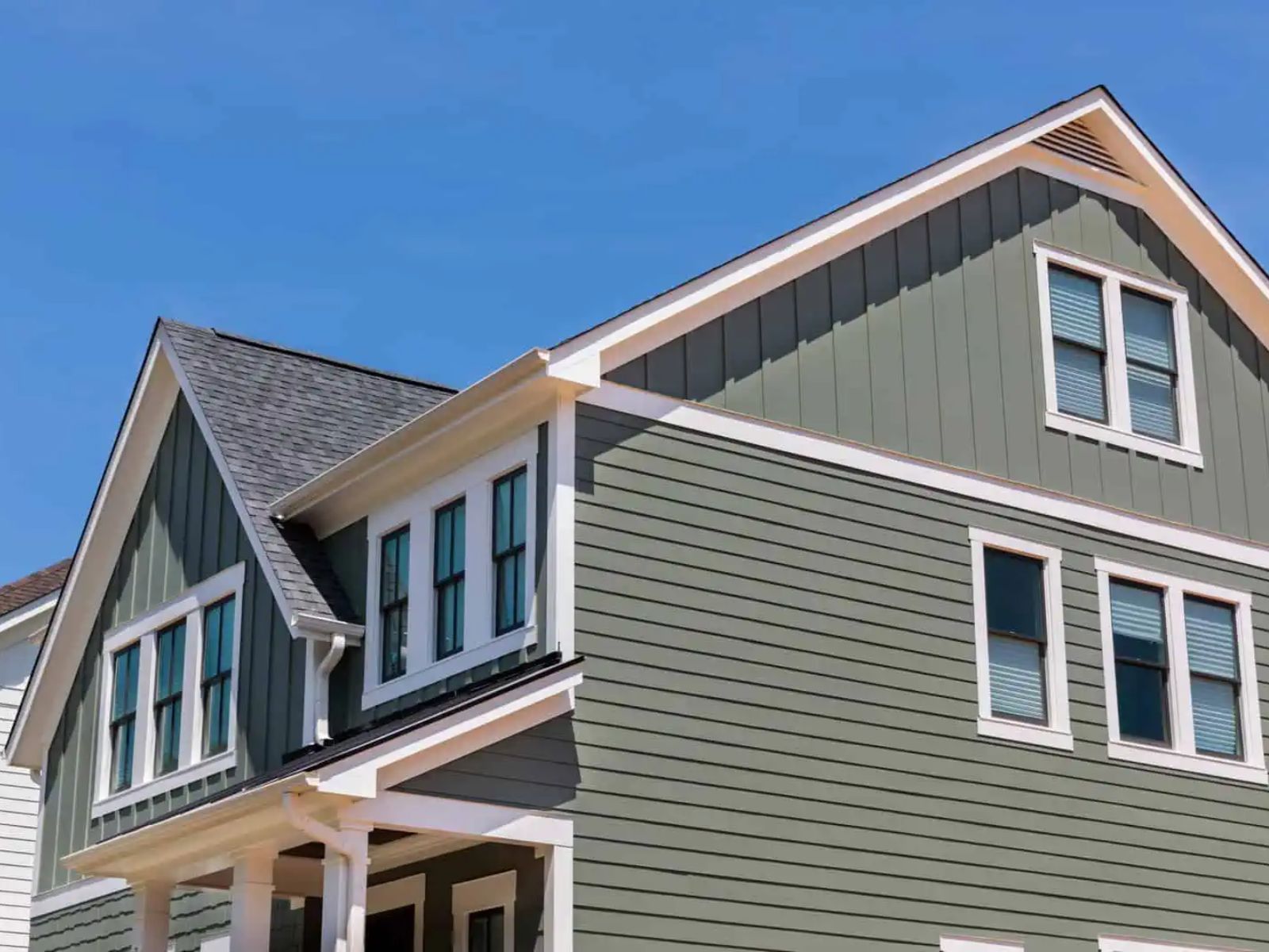 Two-story residential home with architectural shingle roof, gable design, and modern siding under a clear blue sky