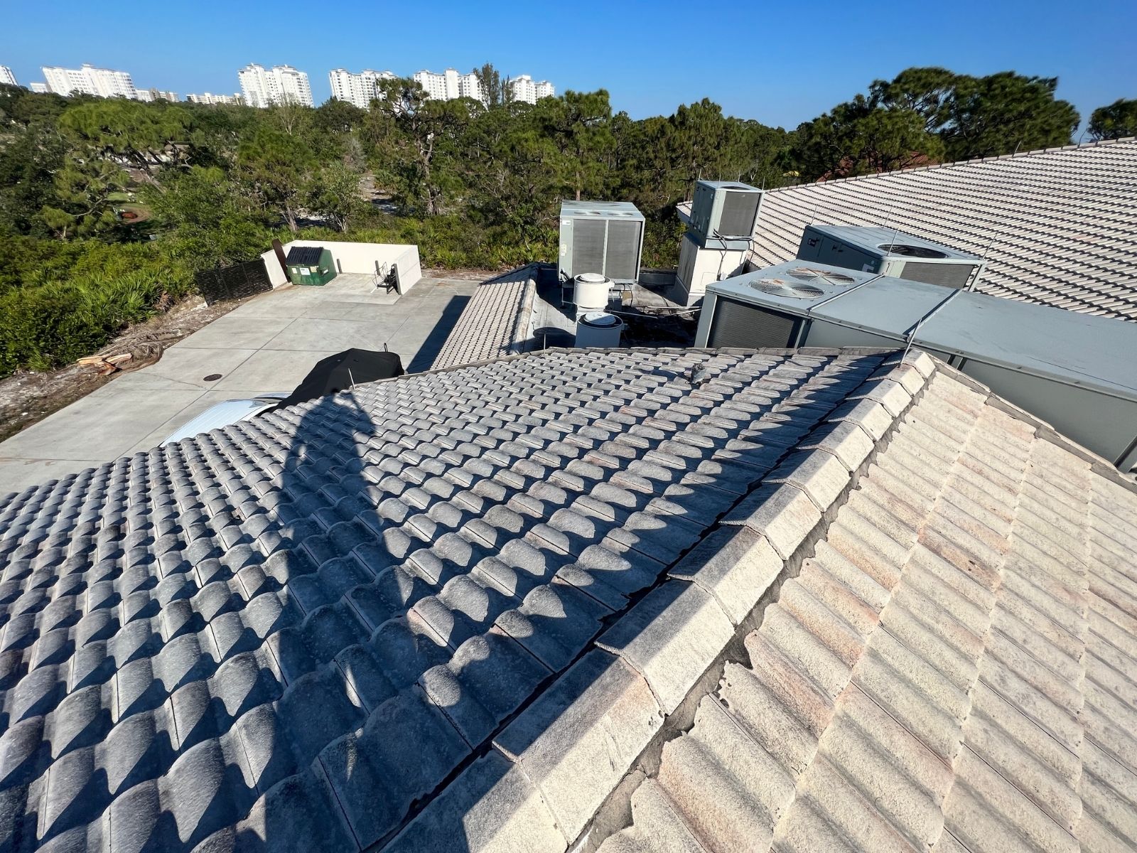 Concrete tile roof with visible shadows, showing HVAC units on the rooftop and a clear blue sky in the background.