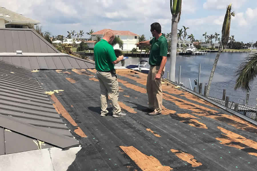 Two kelly roof employees inspecting a damaged metal roof