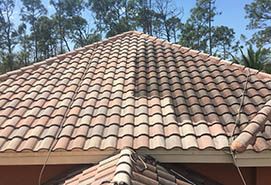 A tile roof being cleaned.  The part that hasn't been cleaned yet is very dark and nasty looking.