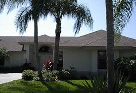 Brown shingles on home with green lawn and palm trees.