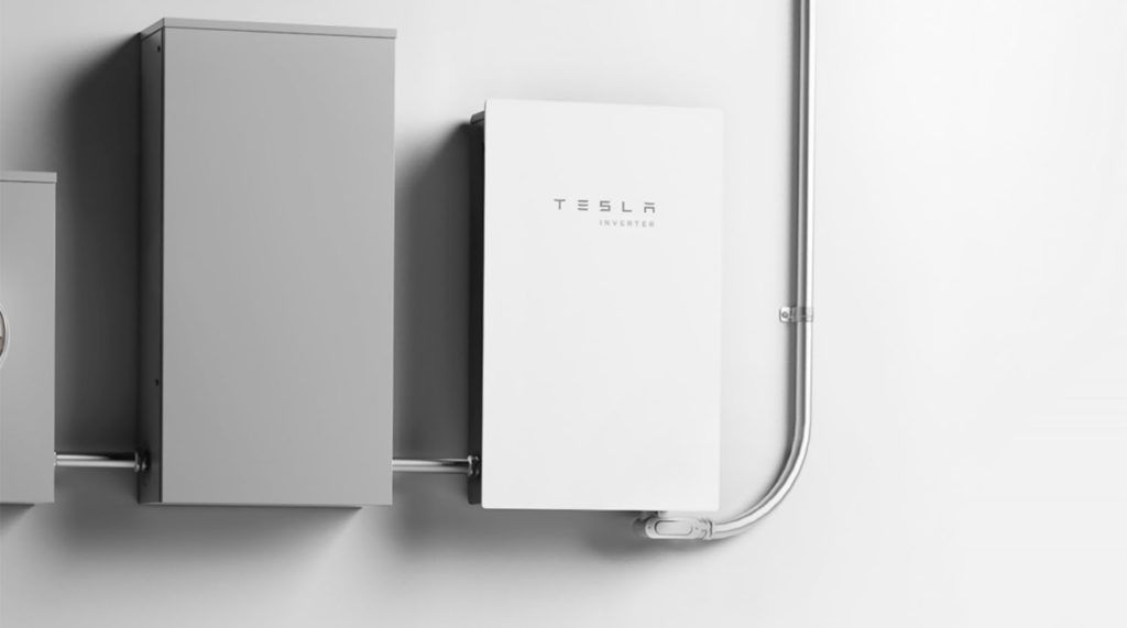 A Tesla Solar Inverter along side a traditional breaker box and power meter.