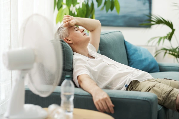 Homeowner sitting on a couch in front of a fan, overheated from a home that is not holding its cool air