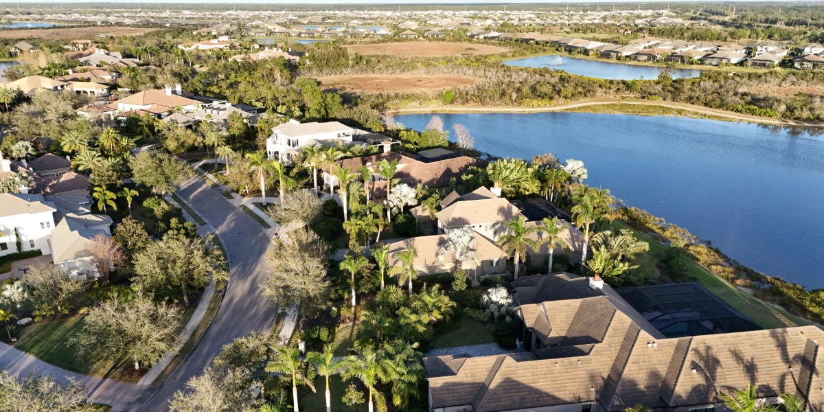 Aerial view of a Florida neighborhood with shingle roofs, tile roofs, palm trees, and a lake