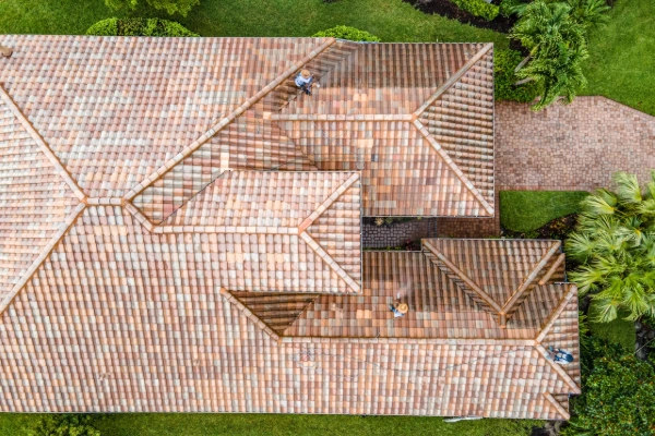 Overhead view of workers cleaning a large tile roof with multiple hips and valleys